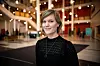 En kvinne poserer foran et stort, moderne atrium med hengt belysning og mørke gulv.