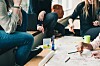 Gruppe som arbeider sammen rundt et bord med skisser, notater, tusjer og bærbare datamaskiner.
