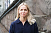 Blond kvinne i mørkeblå genser foran en gammel steinvegg.