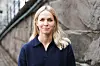 Blond kvinne i mørkeblå genser foran en gammel steinvegg.