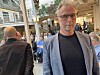 Mann med briller og grå blazer står foran en gruppe mennesker i et lyst innendørs lokale.